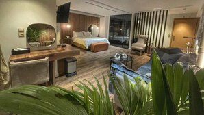 Ein modernes Hotelzimmer mit Bett, Schreibtisch, Stuhl, Sofa und einem großen Spiegel.