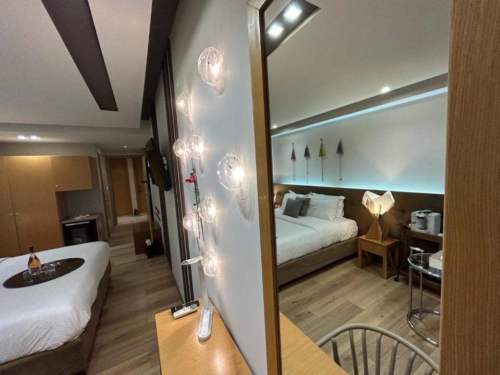 A modern hotel room with a bed, bedside table, lamp, and a wall-mounted shelf with decorative items.
