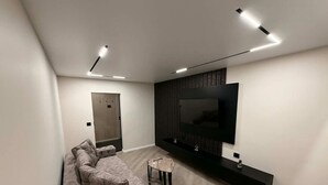 A modern living room with a sectional sofa, a small round table, and a flat-screen TV mounted on a dark wooden panel. - SteRo Luxury Residence | Modern Apt | Self Check-In | Free Minibar (Galați)