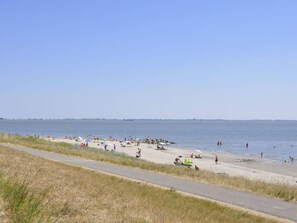 Ein Strand mit gepflastertem Weg, entspannten Menschen und einem wolkenlosen Himmel.