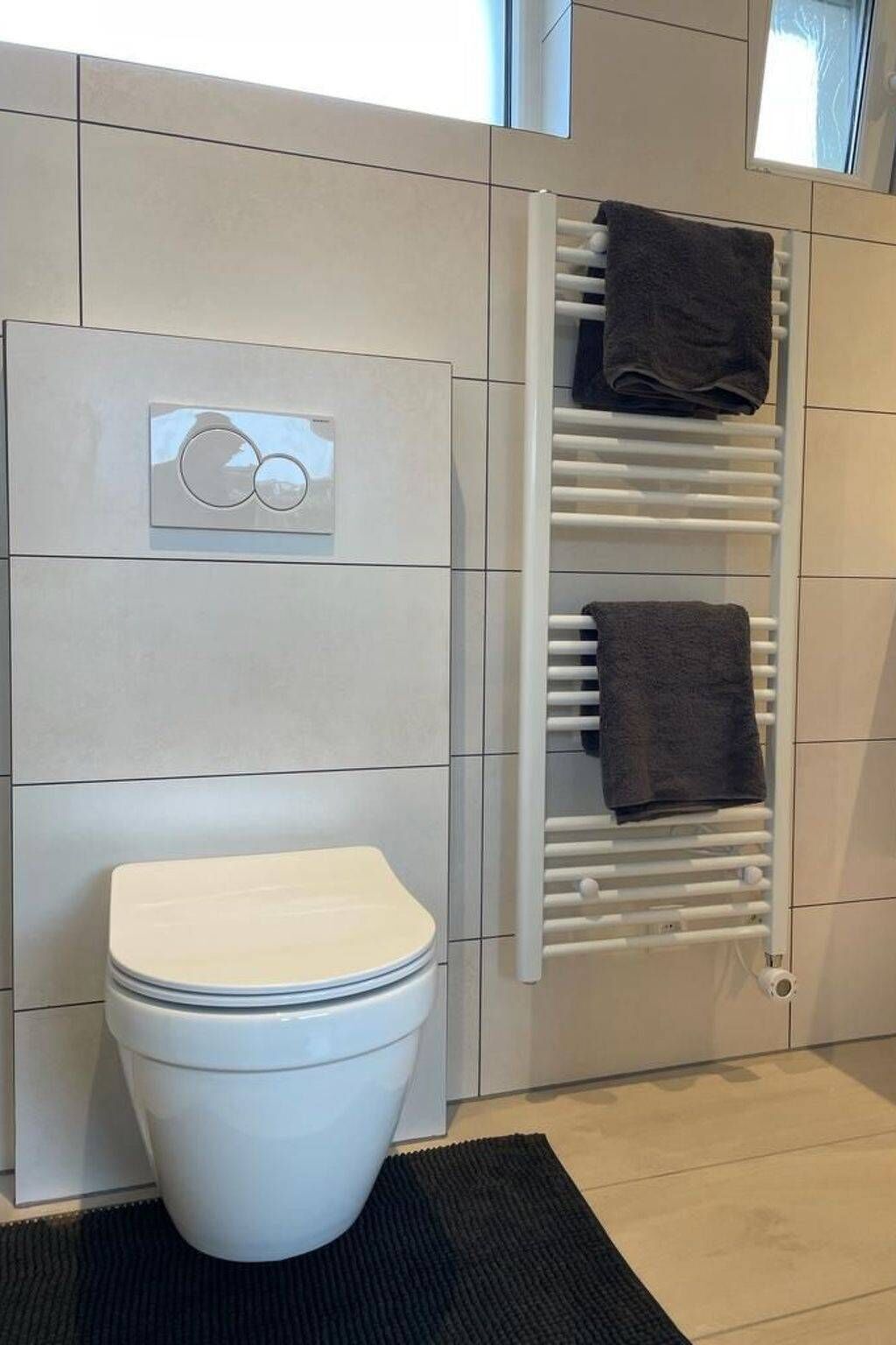A modern bathroom with a toilet, a towel rack, and a built-in heater.