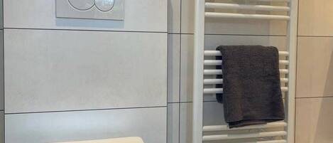 A modern bathroom with a toilet, a towel rack, and a built-in heater.