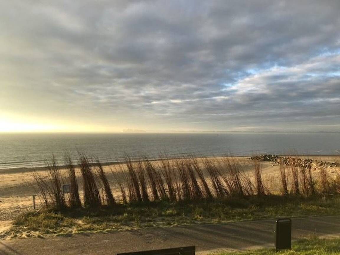Een zandstrand met een pad naar het water, een hek en een brievenbus.