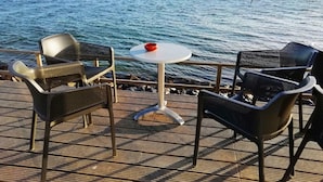 Una terraza con dos sillas de mimbre y una mesa redonda pequeña, con vistas a un mar tranquilo y una costa lejana.
