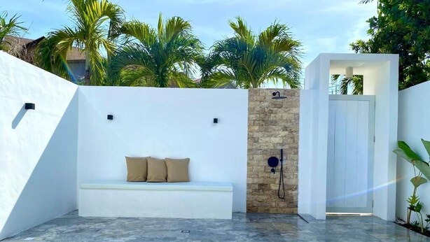 Un área de piscina exterior moderna con un banco blanco y un muro de piedra.