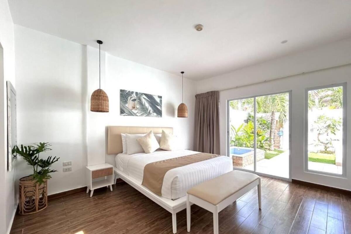 Une chambre à coucher moderne, dotée d’un grand lit, de tables de chevet, d’un banc et offrant une vue sur l’extérieur grâce à de grandes fenêtres.