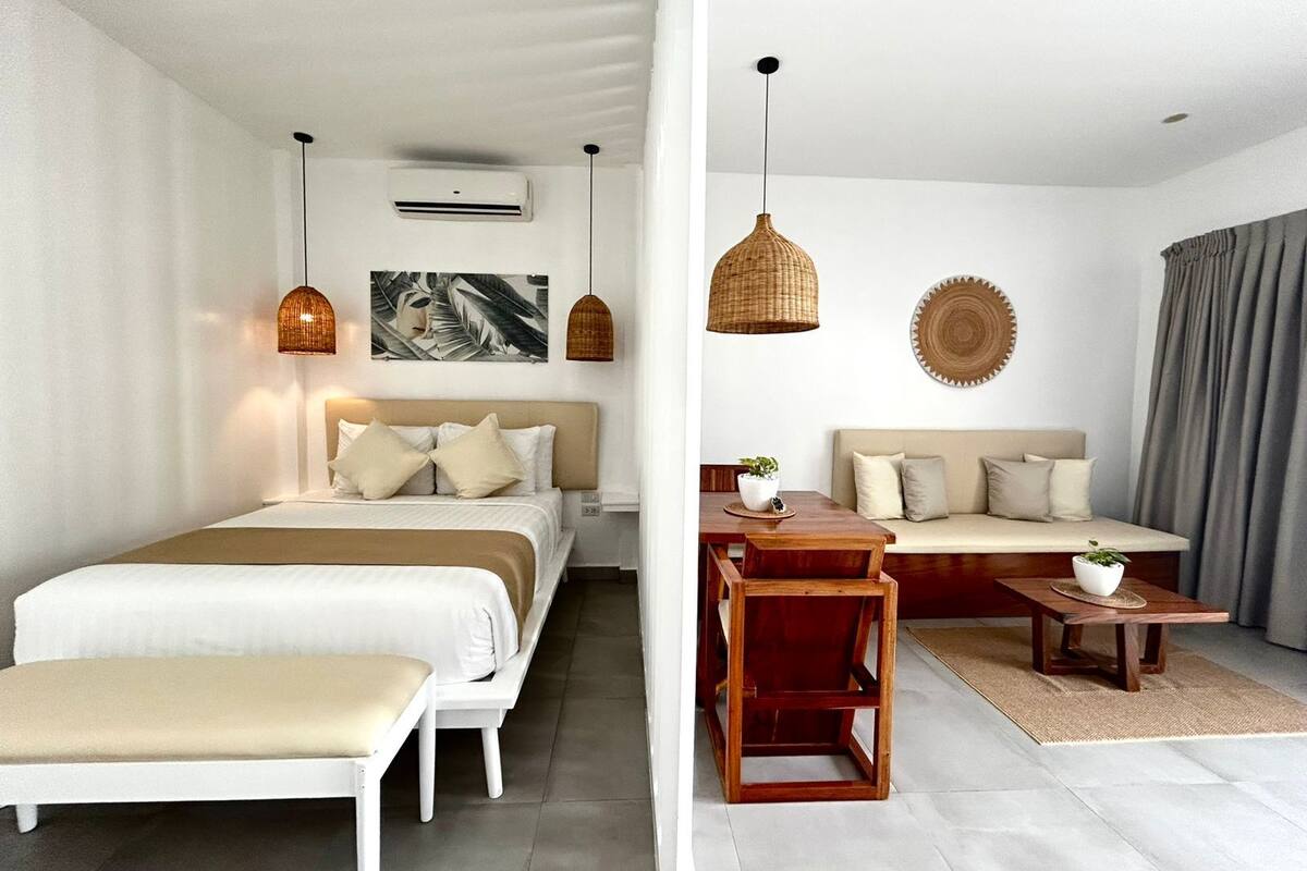 Une chambre d’hôtel moderne comprenant un lit, une table de chevet et un coin salon avec un canapé et une petite table.