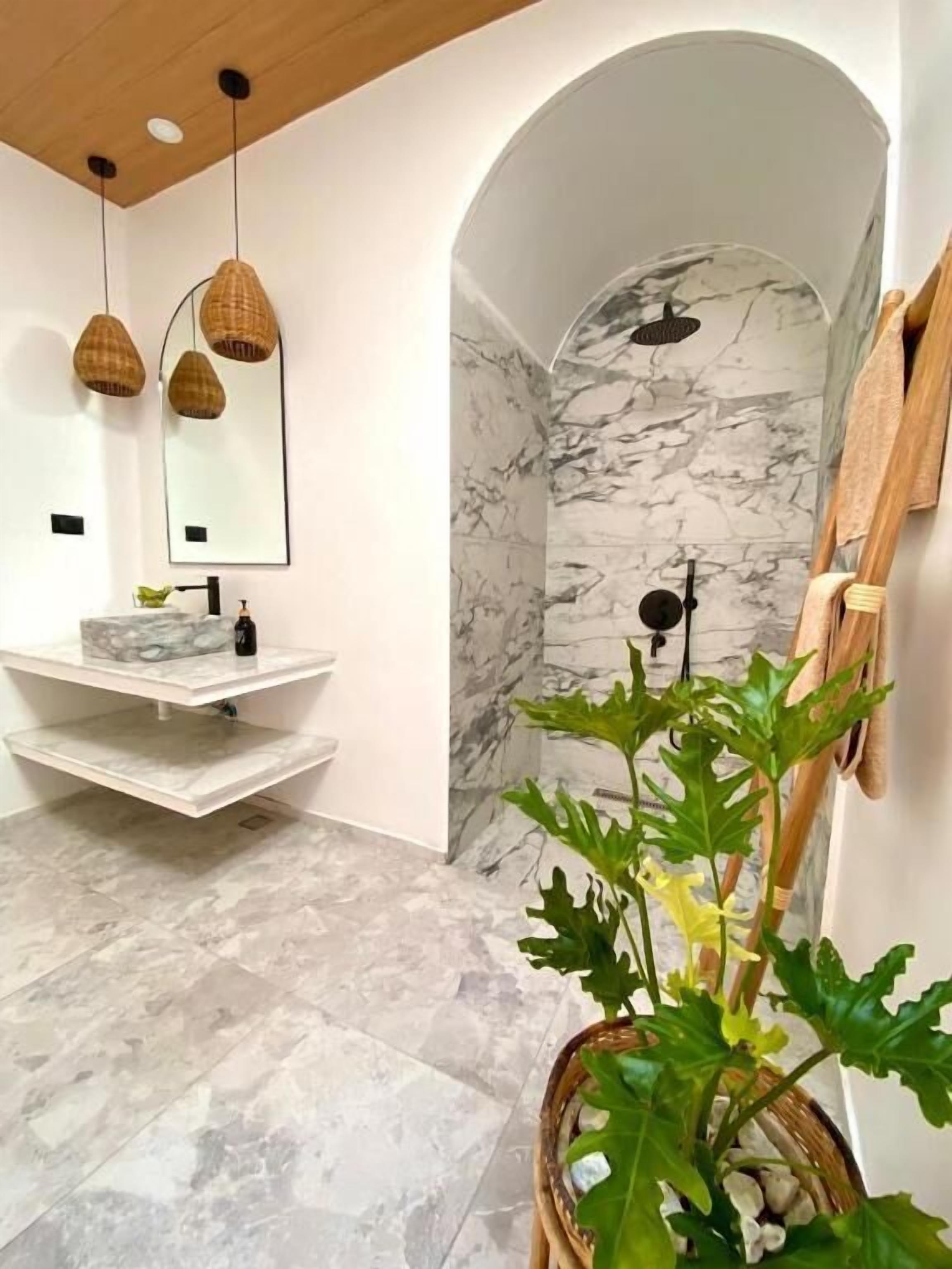 Un baño con tocador de mármol, ducha con pared de mármol y una planta en maceta.