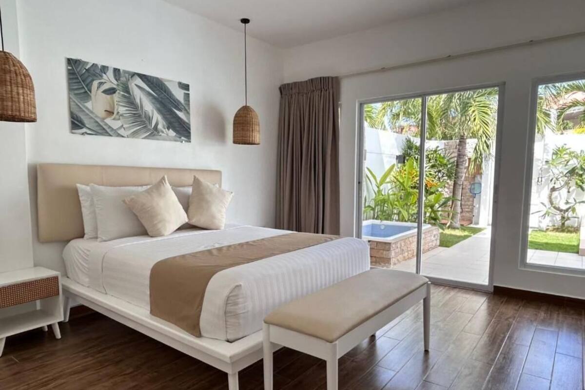 Une chambre à coucher comprenant un lit, un banc, une table de chevet et une grande fenêtre donnant sur un paysage verdoyant.