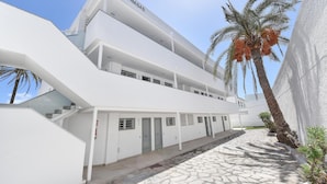 A modern building with a name sign 'LAS NASAS'. It features a multi-level structure with a staircase, a covered walkway, and a palm tree in the foreground. - Cozy Maspalomas Bungalow With Pool (San Bartolomé de Tirajana)