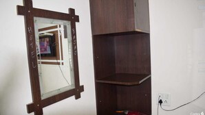 A room with a wooden-framed mirror, a dark wooden shelf unit, and a power outlet.