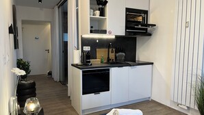 A compact kitchen with a built-in oven, a sink, and a coffee machine. There is a small dining area with a table and chairs. - Apartment in Passau | 23 m² | WLAN | parking space | balcony | BEYOND STAYING (Passau)