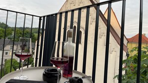 A balcony with a table set for two, featuring a bottle of wine, a glass, and a small black object. - Apartment in Passau | 23 m² | WLAN | parking space | balcony | BEYOND STAYING (Passau)