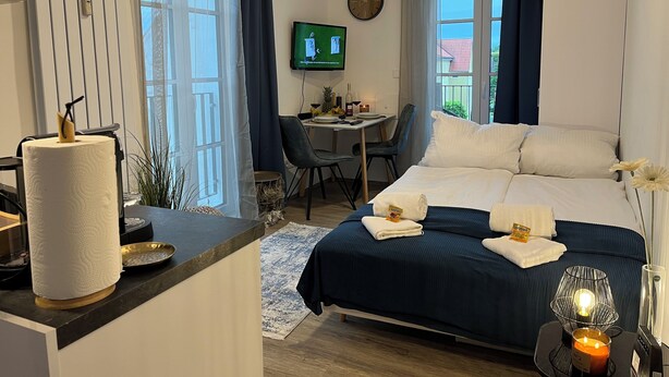 A hotel room with a bed, a desk, a TV, and a window with curtains. - Apartment in Passau | 23 m² | WLAN | parking space | balcony | BEYOND STAYING (Passau)