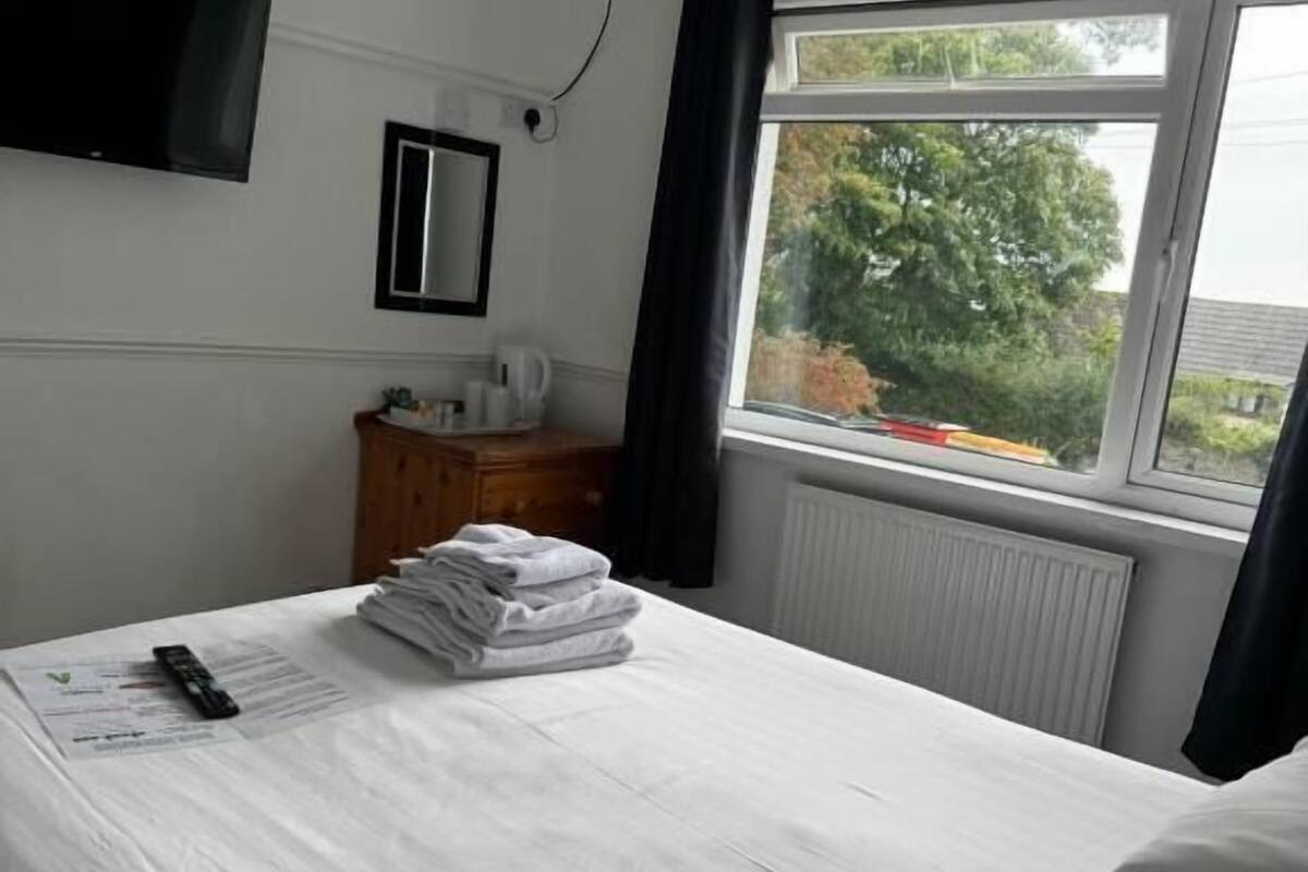 A hotel room with a bed, a flat-screen TV mounted on the wall, a window with curtains, and a radiator.