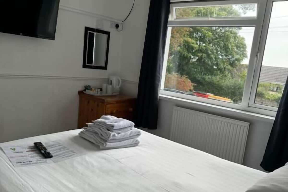 A hotel room with a bed, a flat-screen TV mounted on the wall, a window with curtains, and a radiator.