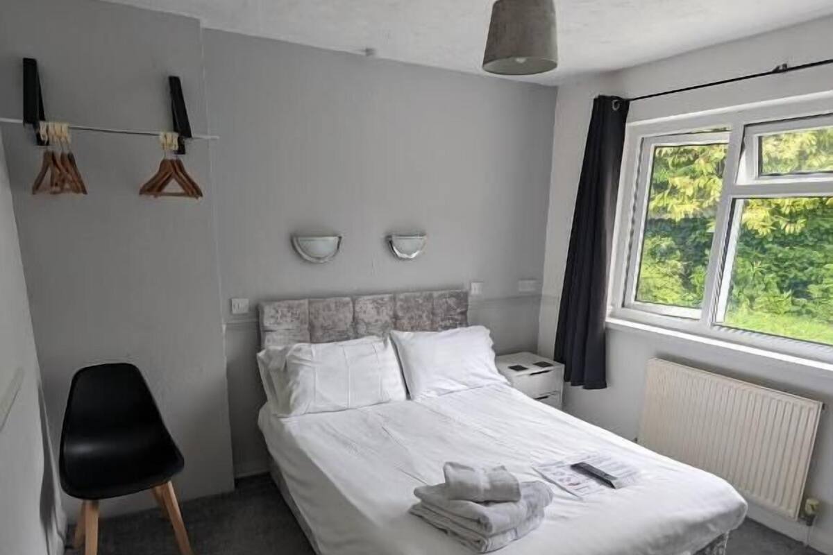 A bedroom with a bed, a chair, a nightstand, a window, and a radiator.