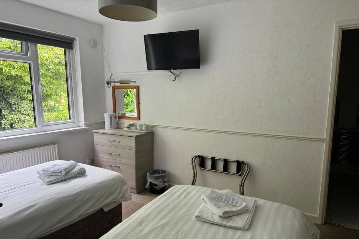 A hotel room with two beds, a television mounted on the wall, and a window providing a view of greenery outside.