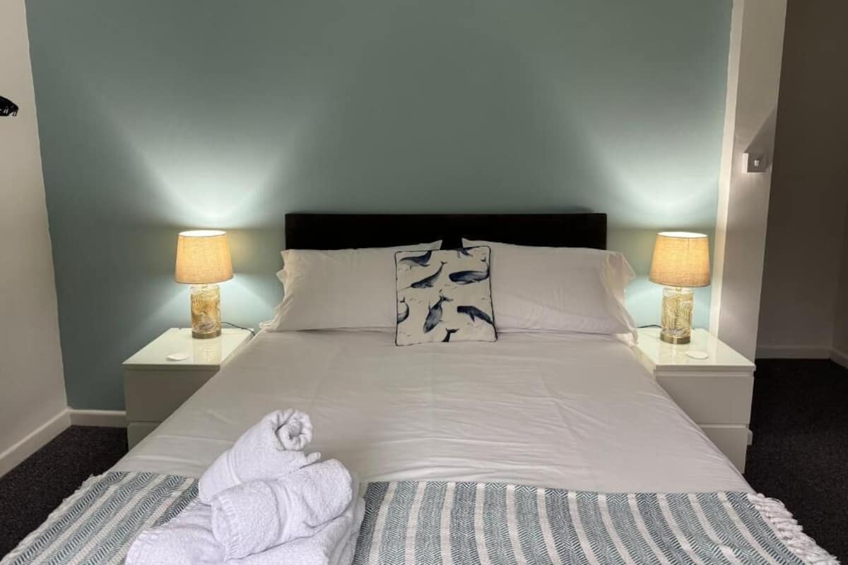 A neatly made bed with a white comforter and two pillows, a striped throw blanket, and a folded towel on the bed.