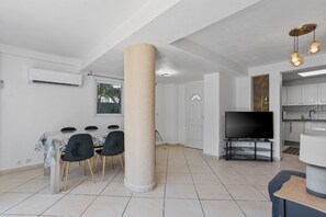 A modern living room with a dining area, a large pillar, a television, and a kitchen area. - Courtille Plage – Natural Retreat by the Sea in Fréjus (Fréjus)