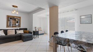 A modern living room with a dark sofa, a glass dining table, and a large window. - Courtille Plage – Natural Retreat by the Sea in Fréjus (Fréjus)