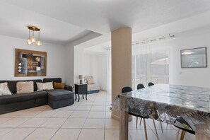 A modern living room with a dark sofa, a glass dining table, and a large window. - Courtille Plage – Natural Retreat by the Sea in Fréjus (Fréjus)