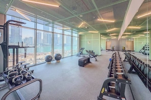 Ein Fitnessstudio mit Trainingsgeräten, großen Fenstern und Blick auf eine Stadtlandschaft.