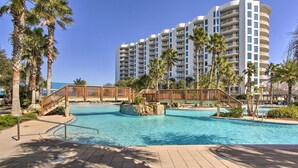 A resort with a large swimming pool, palm trees, and a multi-story building in the background. - Palms of Destin Condo w/ Lagoon Pool (Destin)