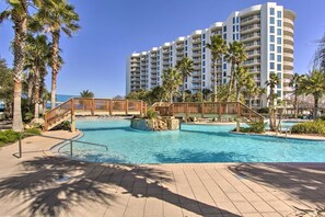 Ein Resort mit großem Schwimmbecken, Palmen und einem mehrstöckigen Gebäude im Hintergrund.