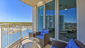 A balcony with wicker furniture, a glass table, and a view of a swimming pool and buildings. - Palms of Destin Condo w/ Lagoon Pool (Destin)