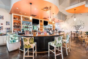 Una cafetería con una barra curva, taburetes con motivos de hojas e ilustraciones de plantas en la pared.