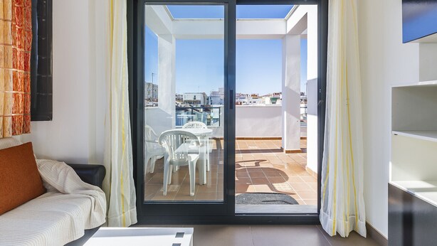 Een moderne woonkamer met een bank, een eettafel met stoelen en een schuifpui die uitkomt op een balkon met uitzicht op de stad.