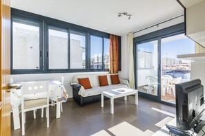 A modern living room with a sofa, coffee table, and TV, large windows with curtains, and a balcony with outdoor furniture. - ATICO EDIFICIO ARAGÜEZ (Torre del Mar)