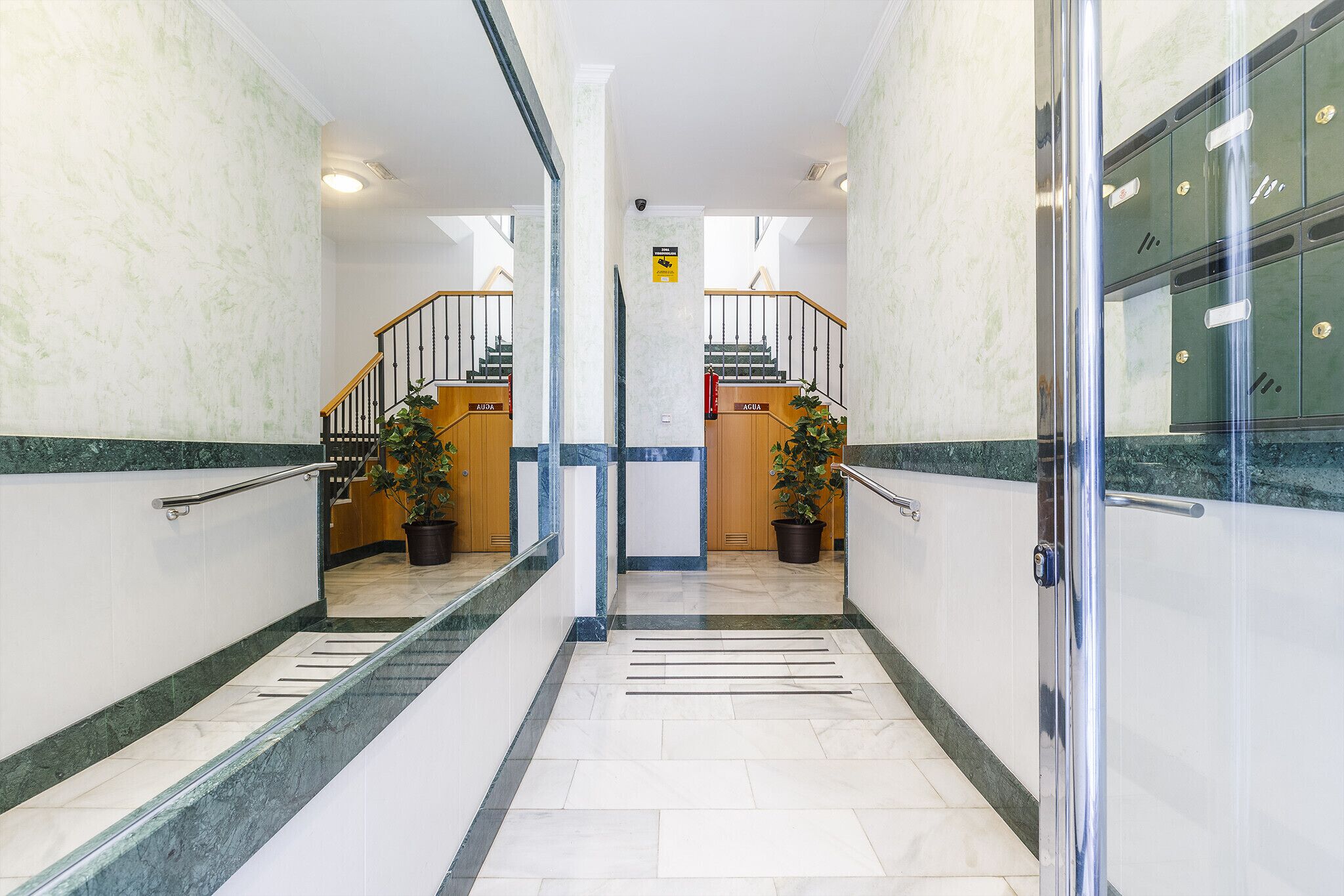 A hotel lobby with marble flooring, a central staircase, and a glass door leading to a room.