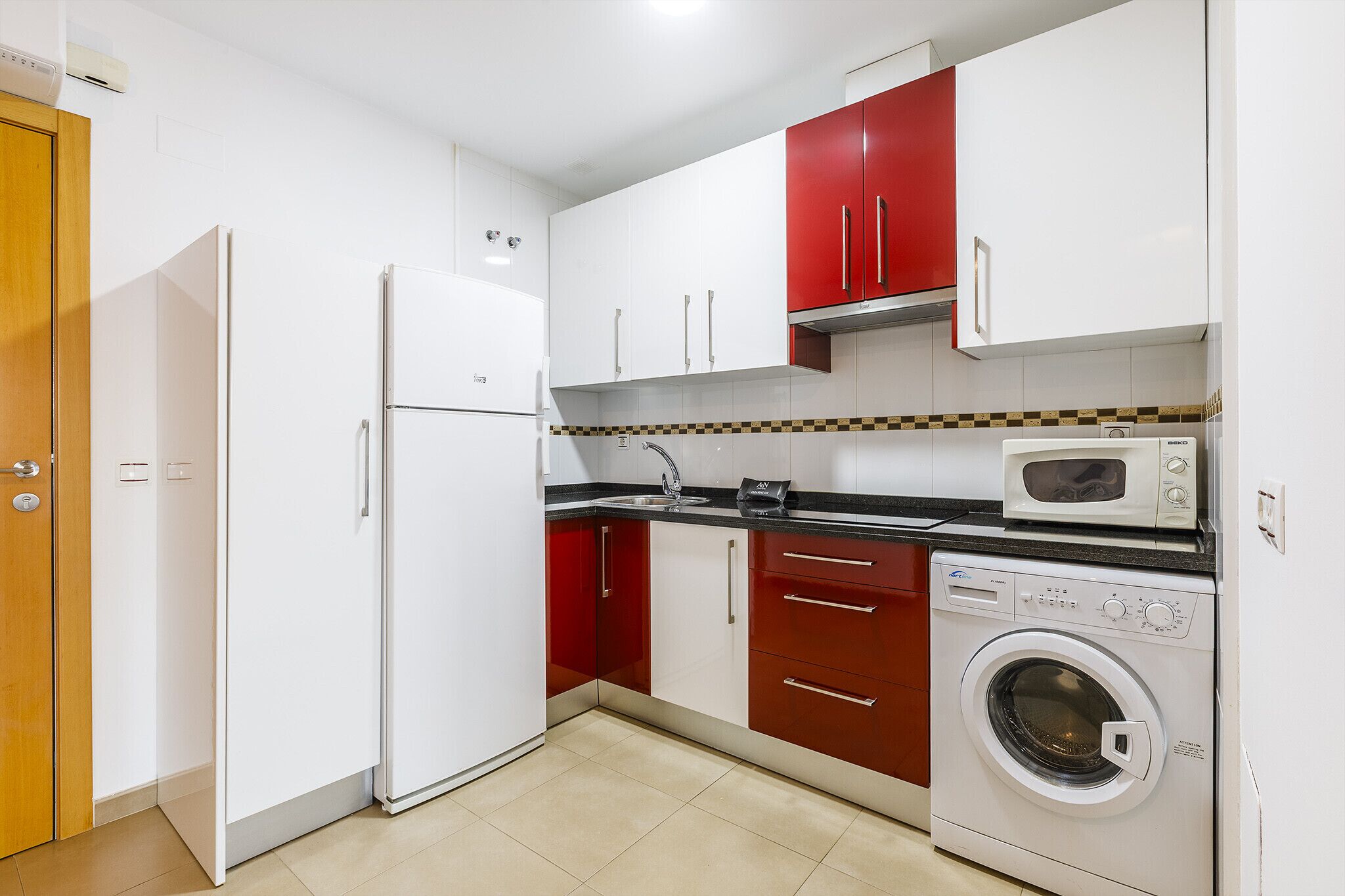 Een kleine keuken met een koelkast, magnetron, oven en wasmachine.