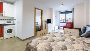 Ein Hotelzimmer mit Bett, Fernseher, rotem Sessel, Sofa, Waschmaschine und Blick auf die Stadt.