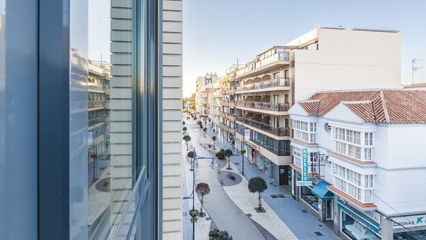 Ein modernes Gebäude mit Glasfassade, eine Fußgängerstraße mit Bäumen und ein Schild für 'MUEBLES TORRES SEA'.