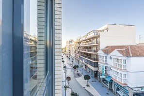Un edificio moderno con fachada de vidrio, una calle peatonal con árboles y un letrero que dice 'MUEBLES TORRES SEA'.
