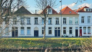 Une rangée de bâtiments blancs aux toits rouges, un canal au premier plan et un ciel dégagé.