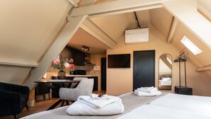 A modern hotel room with a bed, a desk, a chair, a mirror, and a kitchenette in the background. - Just a few minutes walking from Breda’s city centre, with shops, cafés, restaurants, and nightlife nearby. Close to Breda Central Station. Explore the Grote Markt, enjoy Burgundian dining, and relax on lively terraces, all within walking distance. (Breda)
