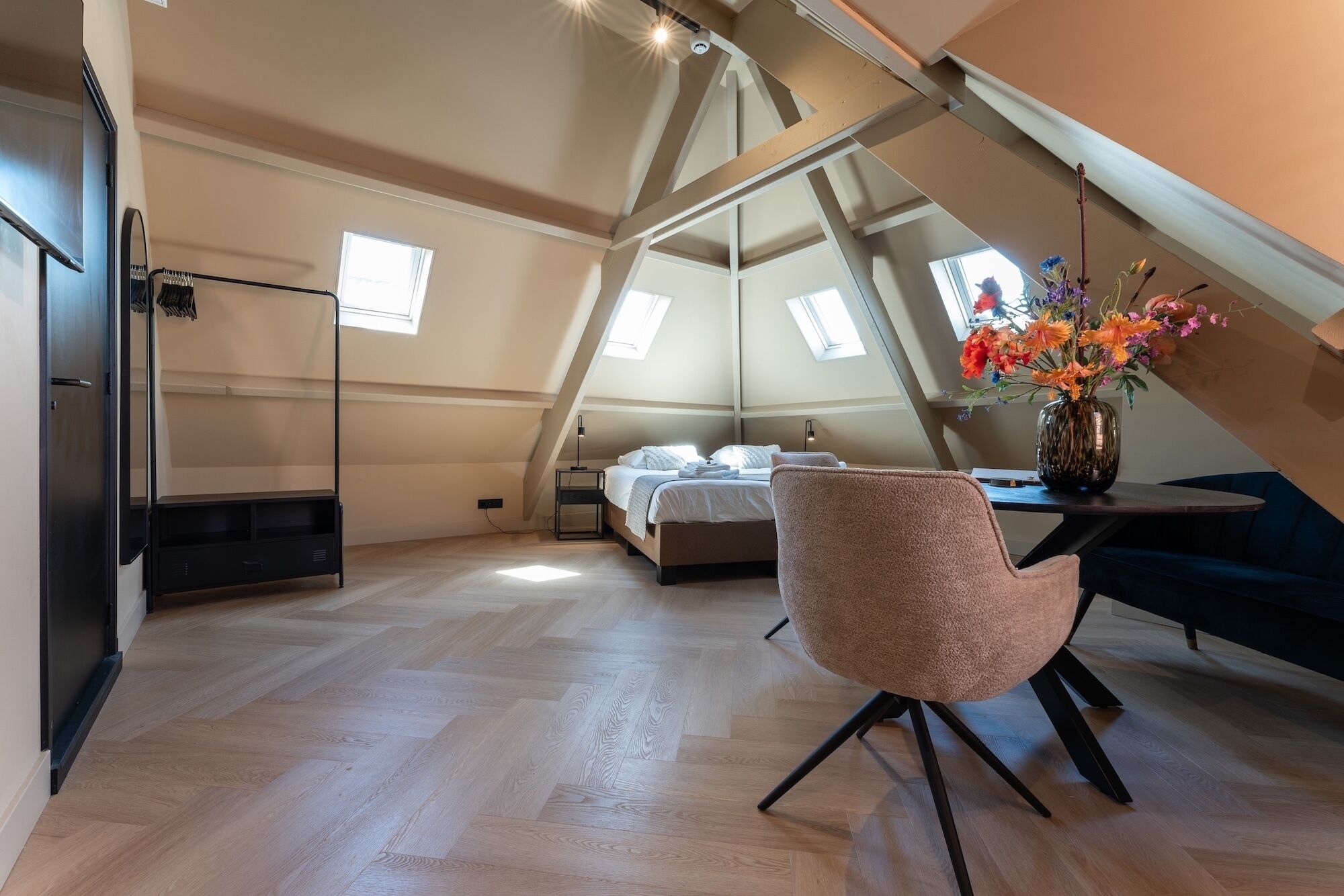 Un dormitorio estilo loft con una cama, una silla, un escritorio y un jarrón de flores.