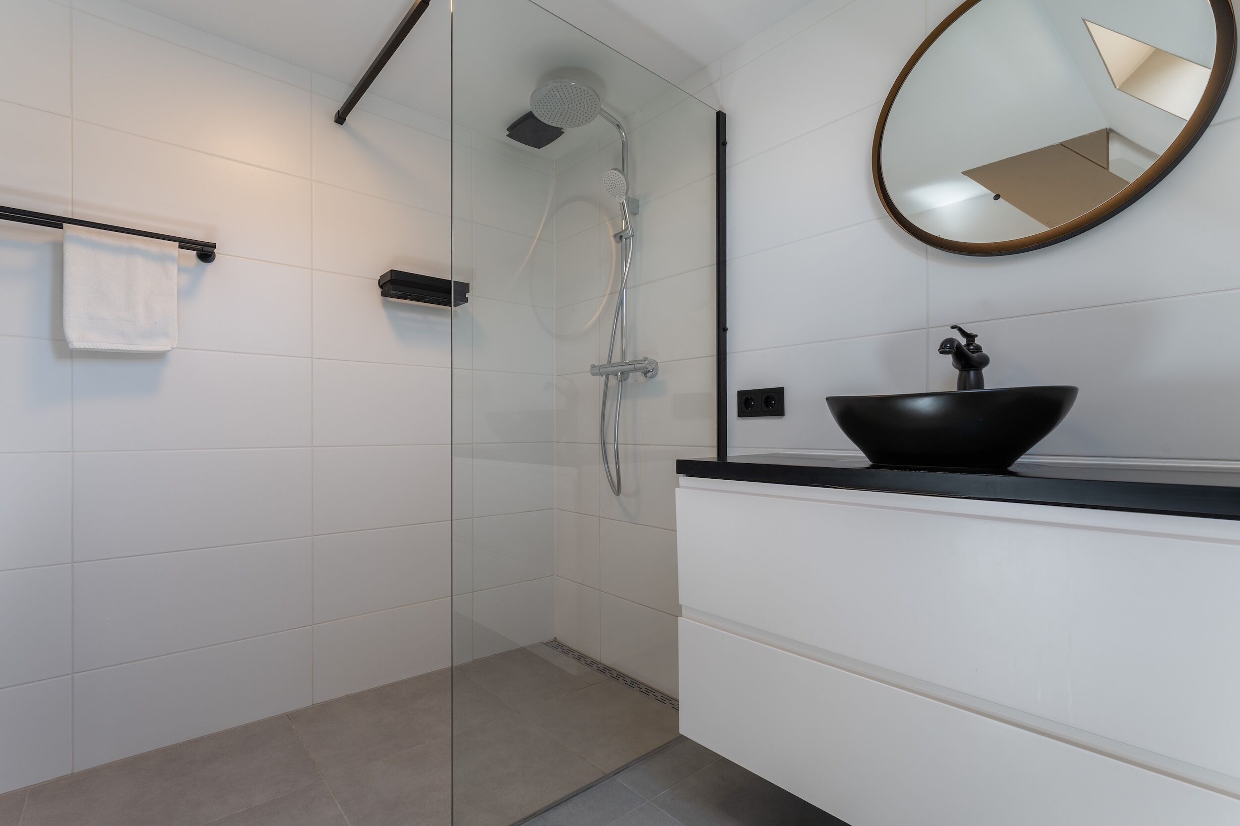 Une salle de bain moderne avec une douche à parois de verre, un lavabo noir et un miroir.