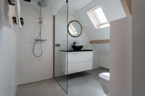 Ein modernes Badezimmer mit Duschkabine aus Glas, einem weißen Waschtisch mit schwarzem Becken und einem Oberlicht über dem Spiegel.