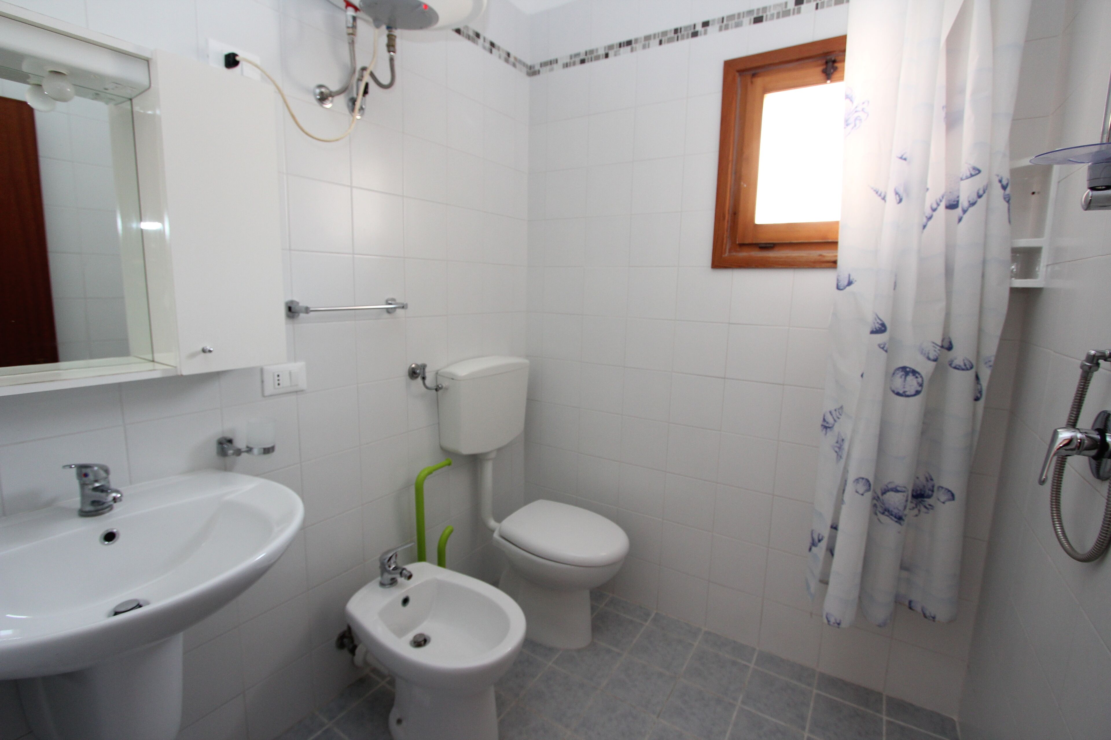 A bathroom with a sink, bidet, toilet, shower, and a window with a curtain.