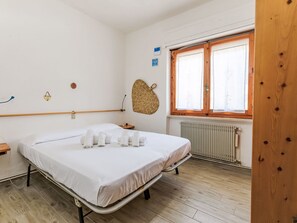 A clean, well-lit room with a bed, a window with wooden frames, a radiator, and a woven wall decoration. - Oleandro by Interhome (Castiglione della Pescaia)
