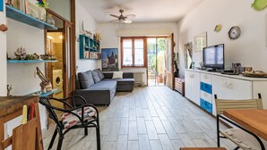 A cozy living room with a sofa, a dining table, and a TV. There are shelves with books and decorative items. - Oleandro by Interhome (Castiglione della Pescaia)
