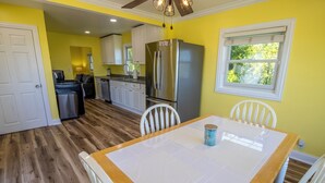 A kitchen with white cabinets, a stainless steel refrigerator, and a dining table with chairs. - Adorable Hilltop Cottage by the Beach (Michigan City)