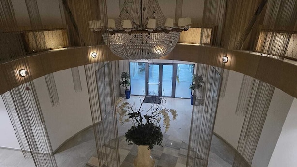 Ein geräumiger Innenhof mit einem beeindruckenden Kronleuchter, einer großen Pflanze im Topf und Blick durch große Fenster nach draußen.