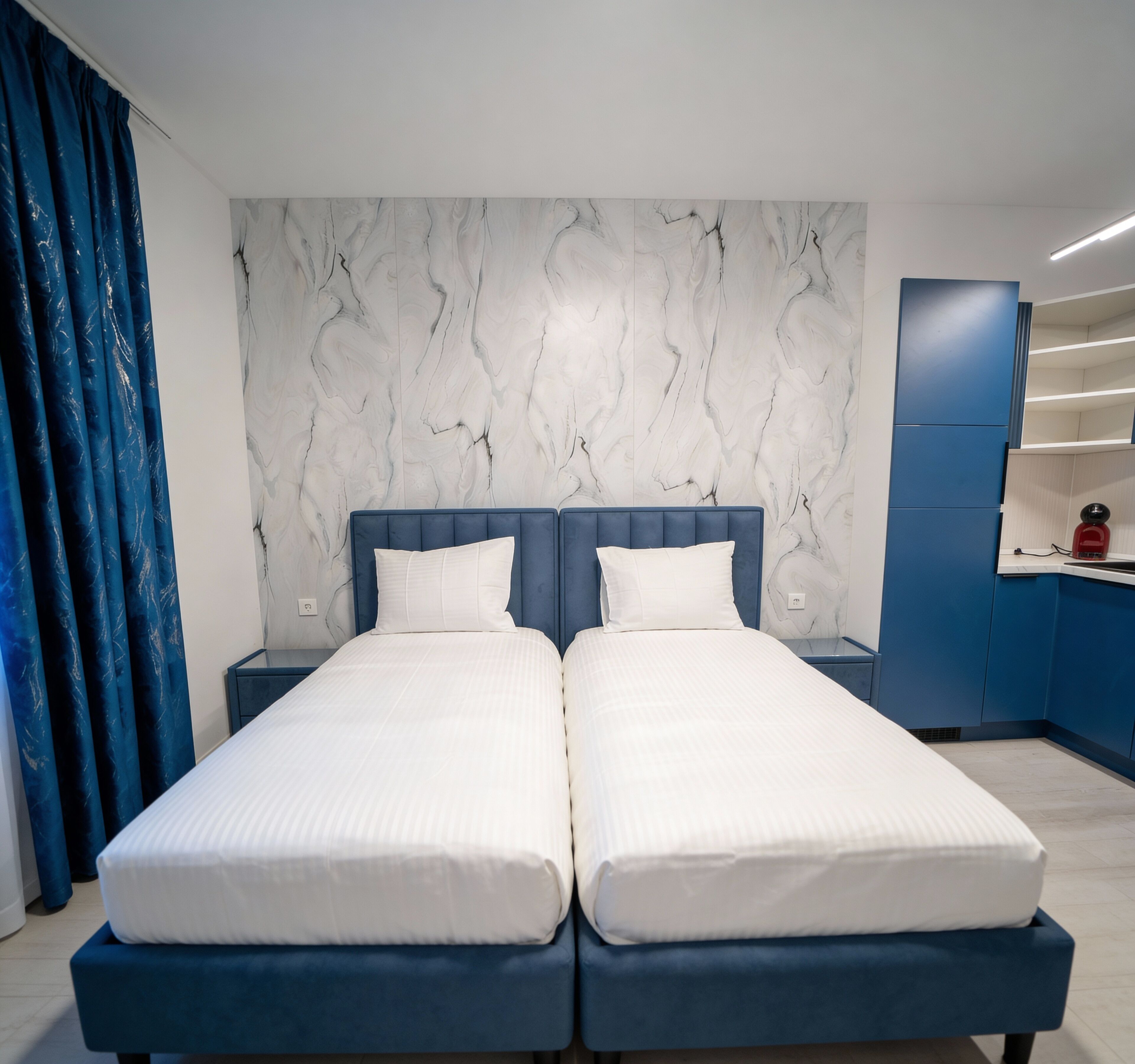 A double bed with a marble-patterned headboard, a blue bedside table, and a blue curtain.