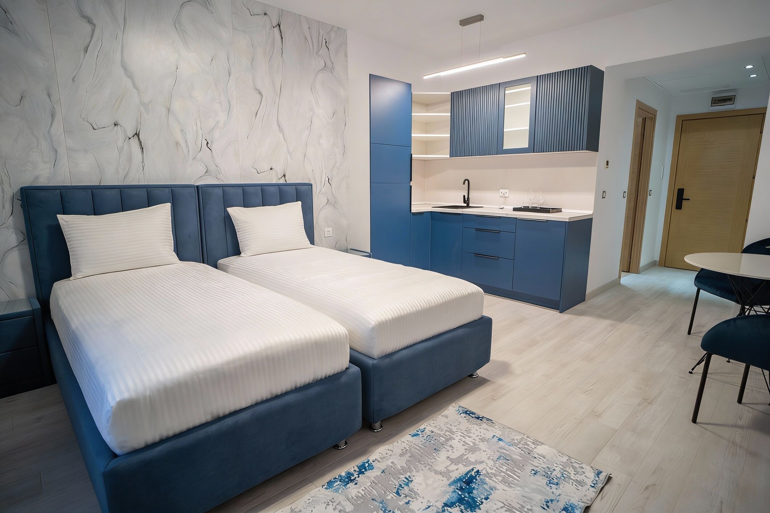 Ett modernt hotellrum med en vägg av marmor, en dubbelsäng, ett litet pentry och en matplats.